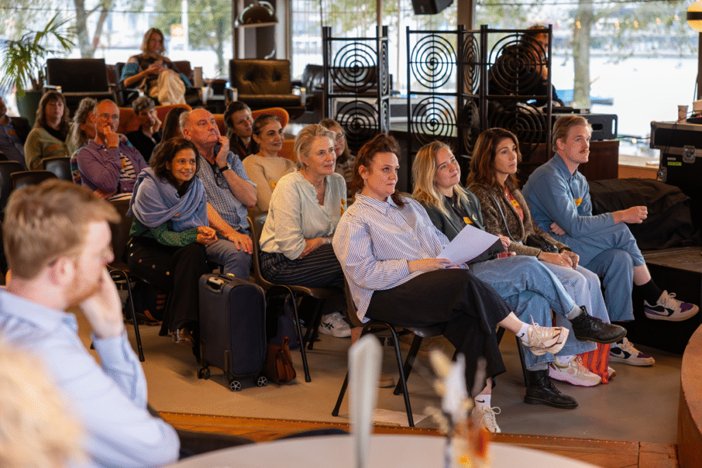 Foto van een zaal mensen in de Tolhuistuin die zitten op stoelen en luisteren naar een presentatie.
