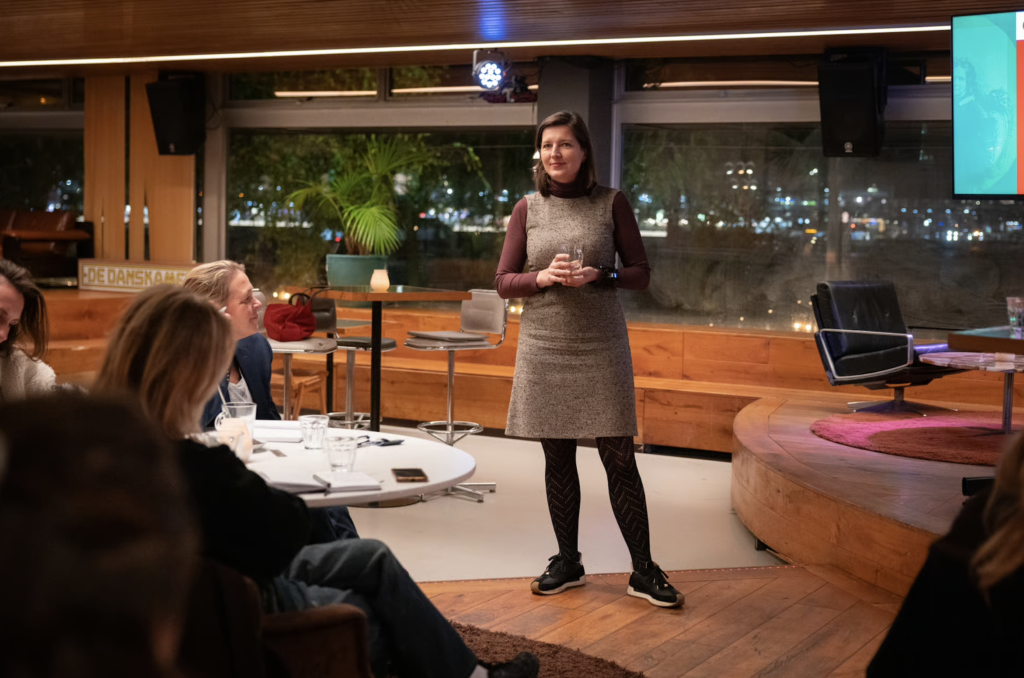 Maartje Duin staat in eventzaal te spreken voor groep mensen